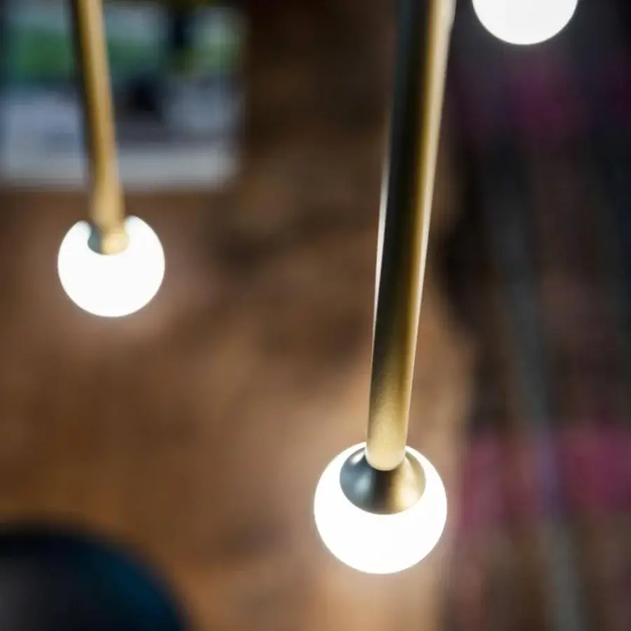 Elegant Penta Storm suspension lamp with cylindrical matte gold metal rods and bright white spherical lights