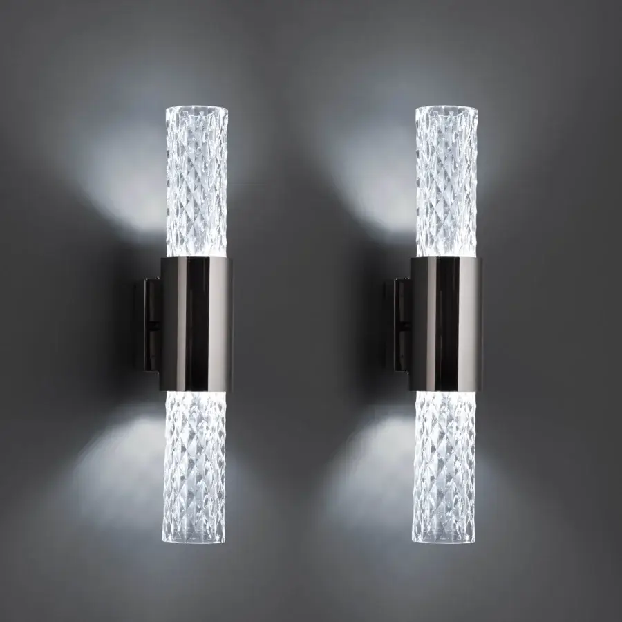 Wall lamps, clear glass facets, dark gray metal housing, cylindrical shape, geometric design, mounted on gray wall, emitting white light.