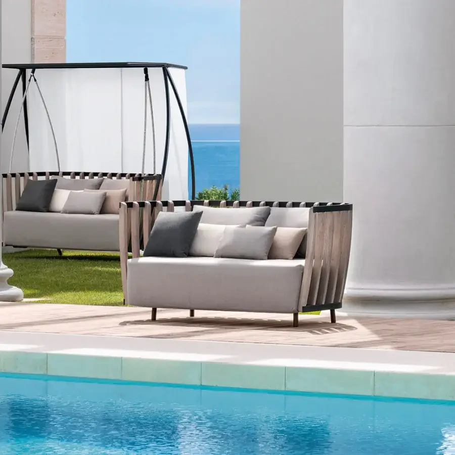 Architectural Ethimo Swing sofa with a metal frame, rhythmic teak slats, and neutral beige upholstery complemented by darker gray cushions