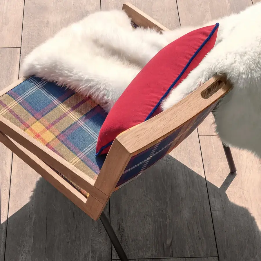 Lavish Ethimo Allaperto lounge chair with plaid textile upholstery, satin-finish wood and vibrant red sheepskin cushion
