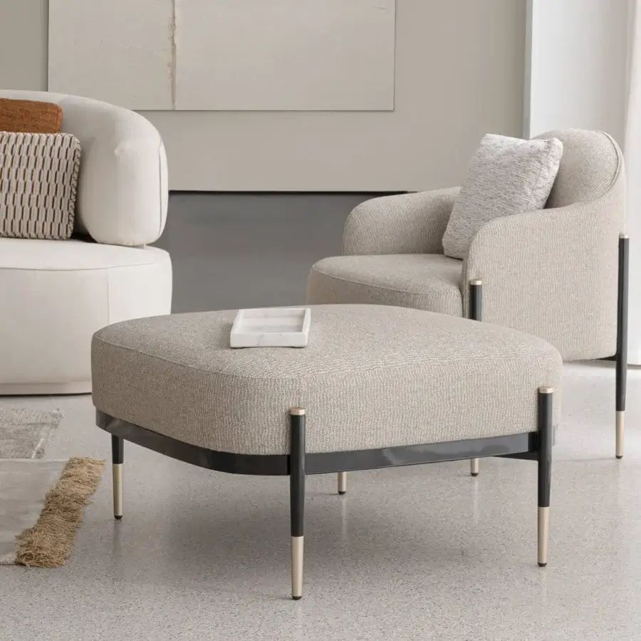 Refined Capital Oxford ottoman with neutral beige fabric upholstery and dark-to-brass metallic legs