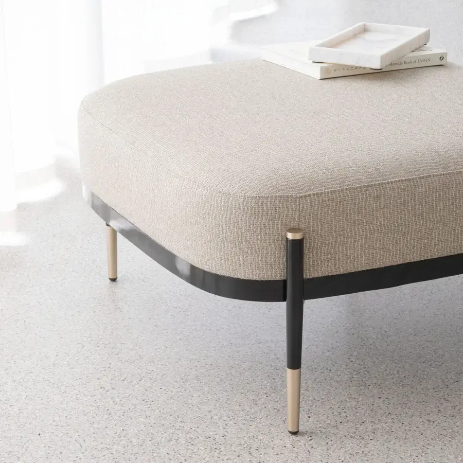 Distinguished Capital Oxford ottoman with gently curved form, neutral beige fabric upholstery and polished brass-detailed metal legs