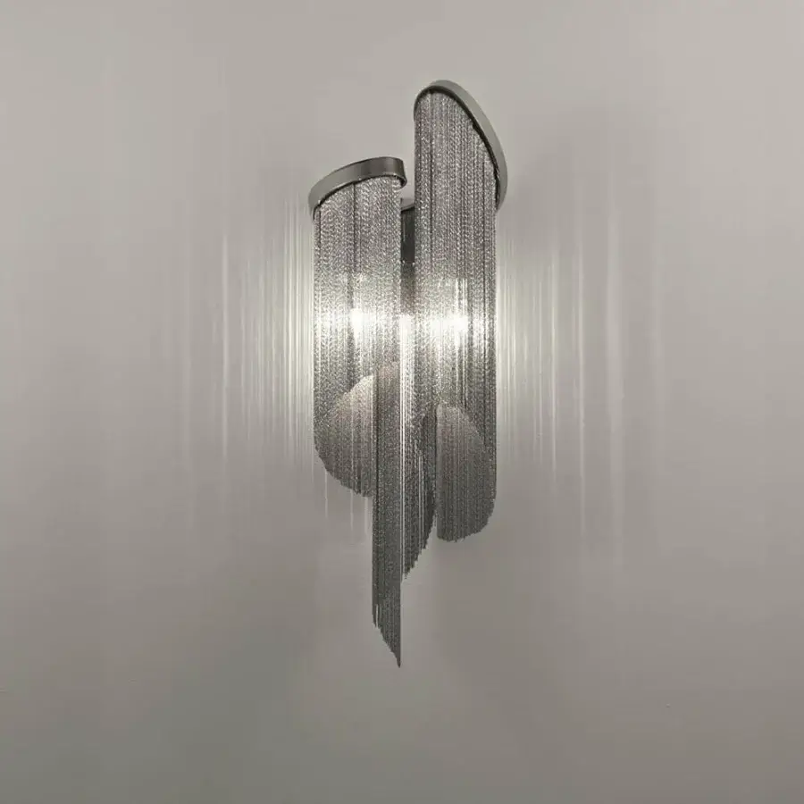 Vertical metallic fixture with hanging strands and curved housings mounted on a light wall surface