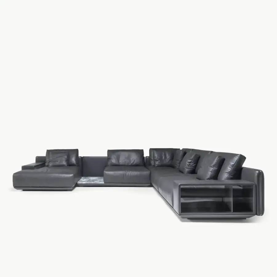 Luxury sectional in grey leather‑like textile with satin sheen, metal backrest, veined stone insert, glass and metal table