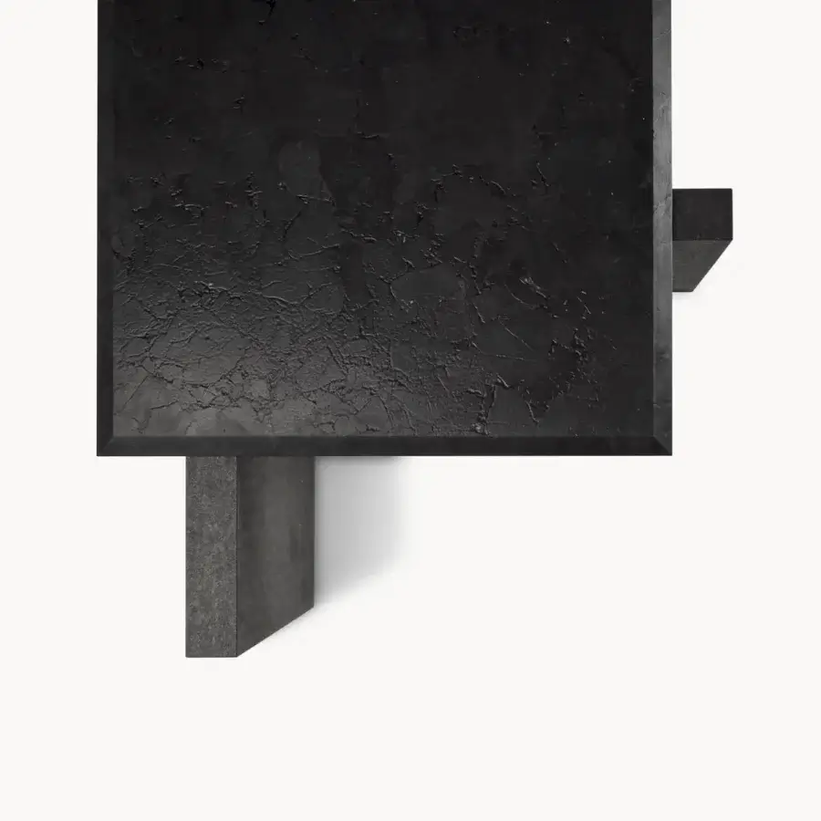 Elegant table with charcoal marble or granite slab, beveled edges, deeply textured matte stone surface and chunky asymmetric supports