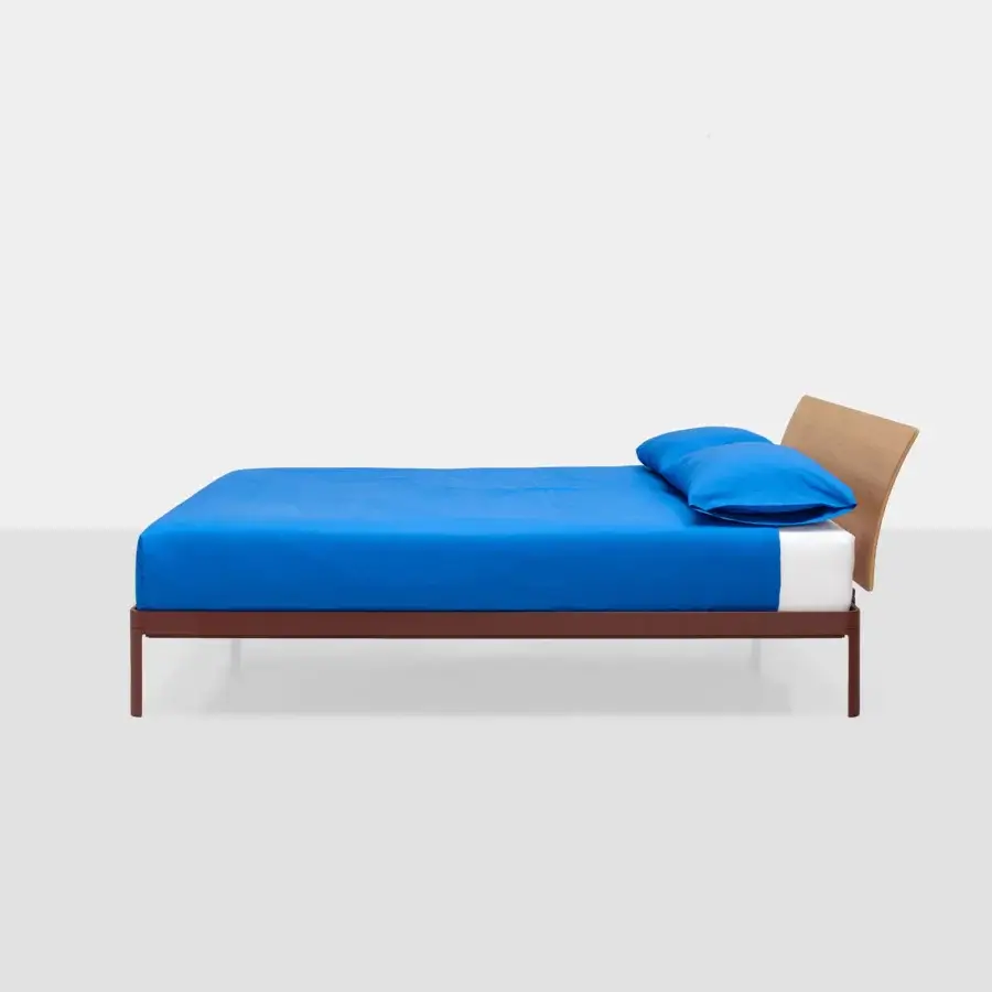 Premium Kristalia AluAlu Bed with matte powder‑coated reddish‑brown metal frame, wood headboard, and vibrant blue bedding