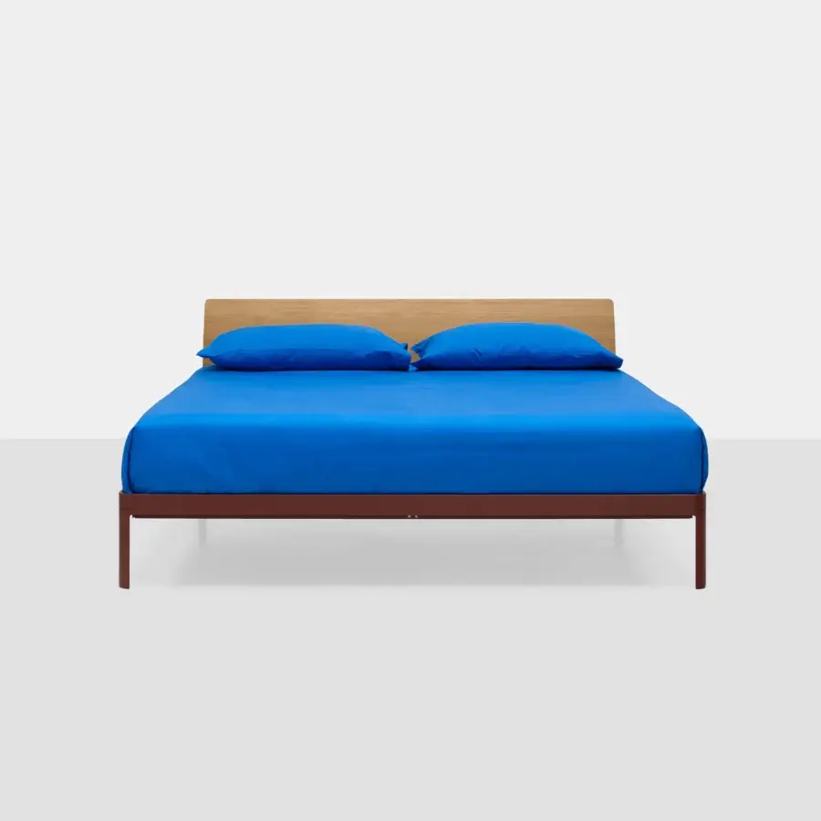 Sophisticated Kristalia AluAlu bed with vibrant blue bedding, matte wooden headboard, and dark reddish‑brown metal legs