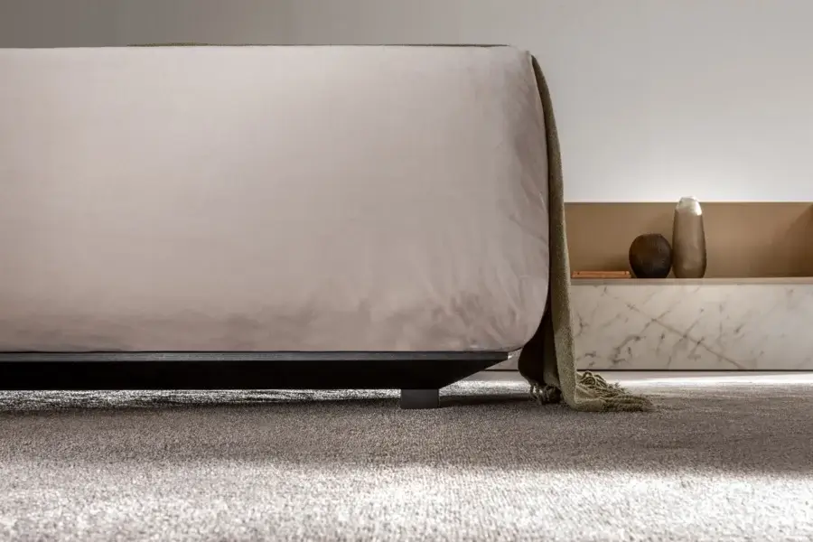High-end Laurameroni Symphony Bed with black aniline‑dyed wood base, velvet headboard in neutral taupe, matte‑finished metal legs, and muted olive‑green textile throw.