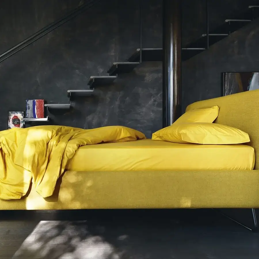 Luxury Noctis Doxy Wide bed in vibrant yellow textile with rounded headboard plus dark smooth metal sled foot supports