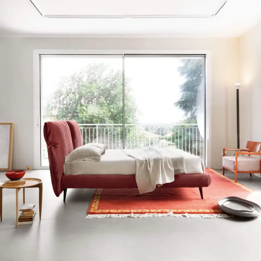 Luxury Noctis Eden Advance bed with curved upholstered headboard, tied bow details, reddish-pink fabric, dark metal legs