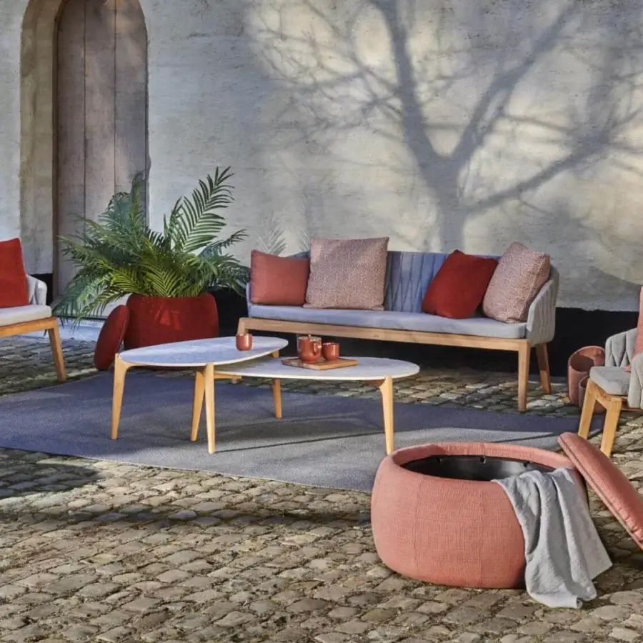 Refined Royal Botania Calypso lounge chair with teak base, stainless steel backrest and light gray textile upholstery accented with reddish-orange cushions