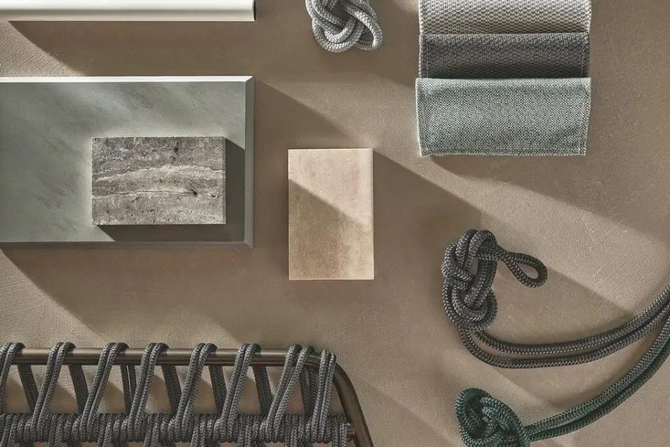 Textural moodboard with teal woven rope, silver metal rods, gray stone tile, beige sandstone, and dark bronze chair detail on taupe background.