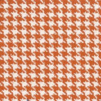 Houndstooth textile with white and burnt orange repeating pattern; woven fabric features irregular four-pointed motifs and a slightly raised texture.
