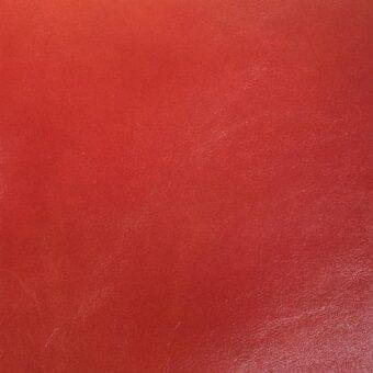 Red leather sample with fine grain texture, displaying warm terracotta tones and subtle surface scratches, evenly lit close-up.
