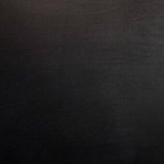 Vegetable-tanned saddle leather sample, nero black, grainy texture, displaying natural tone variations and a slightly uneven surface.