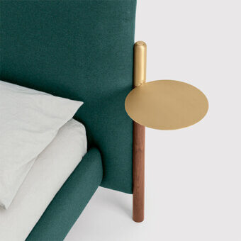 Bolzan Letti bed with teal velvet upholstery, circular brass tray, and dark wood cylindrical support, white linen bedding visible.