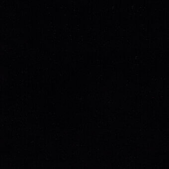 Dark granular texture with scattered points of light, resembling a night sky, dominated by black and subtle variations in tone, photographic composition.