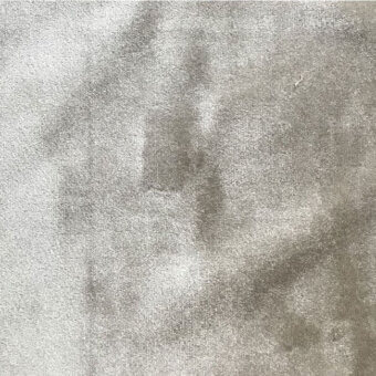 Gray beige velvet fabric texture with mottled shading and a dense short pile, displaying subtle light reflection and uniform surface.