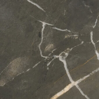 Valentine Grey marble close-up with dark grey base, white veining, and subtle gold lines; polished, dense stone texture.