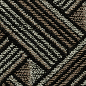 Geometric fabric sample with black, beige, and silver-gray threads displaying diagonal lines and circular elements, with a visible product label.