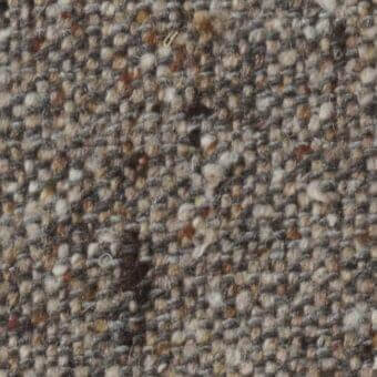 Heathered tweed fabric texture with muted browns, grays, and creams, featuring an irregular nubby weave and vertical selvage edge.
