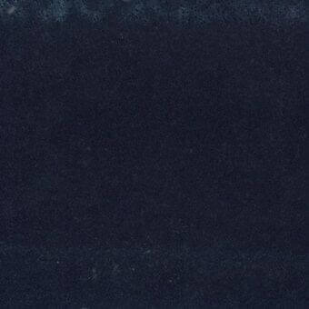 Navy fabric swatch displaying a granular texture, with tonal variations and darker edges suggesting folds, evenly lit for color and texture detail.