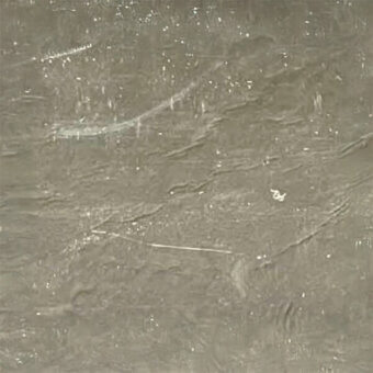 Metallic fabric texture, muted gray “laminato platino” with white speckles, displaying a rippled, diagonally-lined surface and subtle reflectivity.