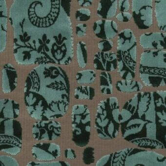 Teal fabric swatch with repeating oval and rectangular shapes, featuring dark green stylized foliage patterns on a taupe background, textured weave.