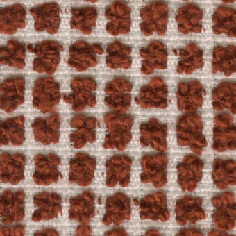 Terracotta textile pattern features a grid of looped-pile squares, creating a raised, floral texture against an off-white woven background.