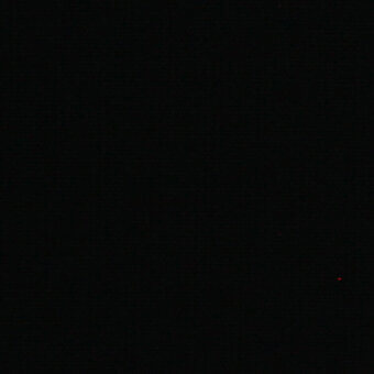 Monochromatic composition of deep black with a single red light point in the lower right, creating stark contrast within a dark, undefined space.