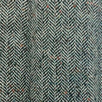 Herringbone tweed fabric, dark green and off-white, repeating V-pattern with orange and brown flecks, dense nubby weave, muted earthy tones.