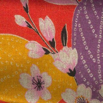 Floral textile pattern with rounded yellow and purple shapes on a red background, featuring pink blossoms and brown branches.