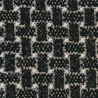 Woven tweed-like fabric texture with black and off-white irregular pattern, dense weave, subtle sheen, and “tammy” p 067 label.