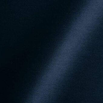 Navy blue fabric swatch with subtle granular texture, diagonal light blue band, and text labels indicating material specification and origin.