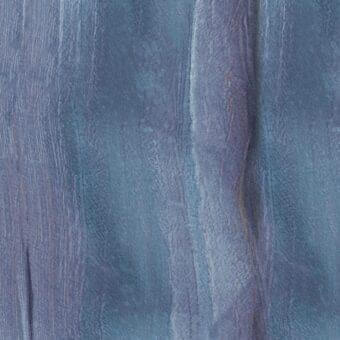 Textured surface of azul macaubas stone with vertical grain, displaying blue and gray marbling, smooth reflective patches, and matte fibrous areas.
