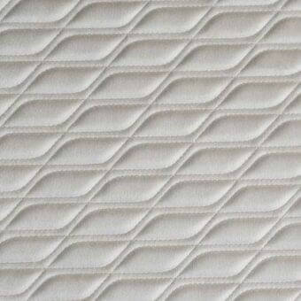 Quilted textile sample in light beige features diagonal, undulating lines forming a chevron motif with fine stitching and a matte finish.