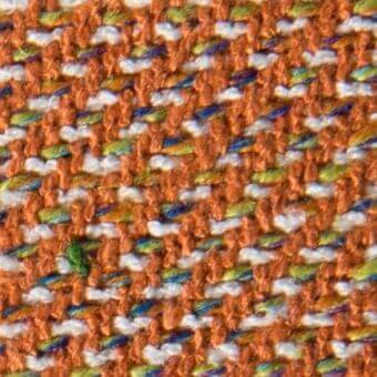 Woven fabric texture, warm orange and off-white twill, dense irregular pattern with green and blue threads, slightly raised nubby surface.