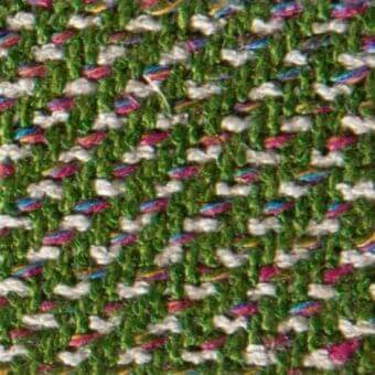 Woven zigzag fabric texture features green, white, pink, blue, and gold hues with a dense, slightly nubby, subtly sheened surface.