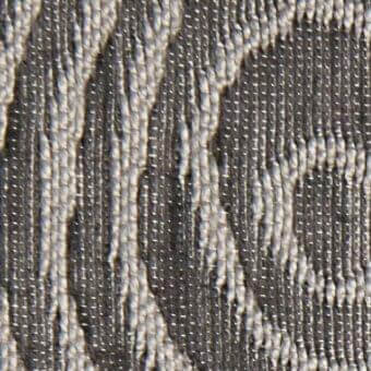 Woven gray fabric texture displays a repeating curved pattern with off-white tonal contrast, featuring visible “verzelloni” fabric identification.
