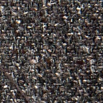 Woven fabric texture, dark gray and beige tones, irregular nubby pattern with embedded particles, subtle text “verzelloni” visible.