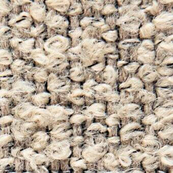 Beige looped pile fabric texture with woven text reading “verzelloni,” displaying a nubby, irregular weave and subtle tonal variations.